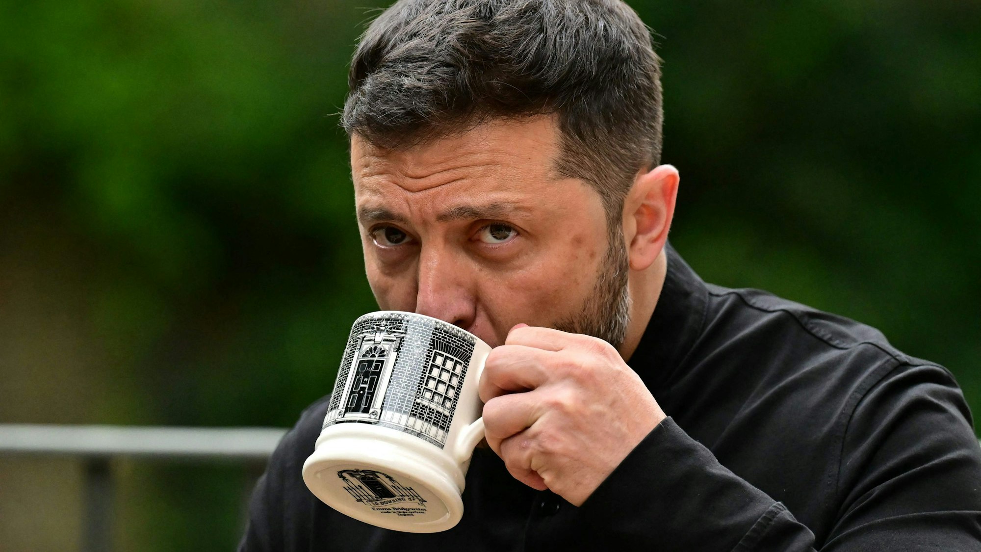 Ukraine's President Volodymyr Zelensky drinks from a Downing Street -themed mug as he sits with Britain's Prime Minister Keir Starmer (unseen) in the garden of 10 Downing Street in central London, on August 14, 2025. Ukrainian President Volodymyr Zelensky met with ally UK Prime Minister Keir Starmer in London on Thursday ahead of a key US-Russia summit in Alaska. (Photo by Ben STANSALL / POOL / AFP)