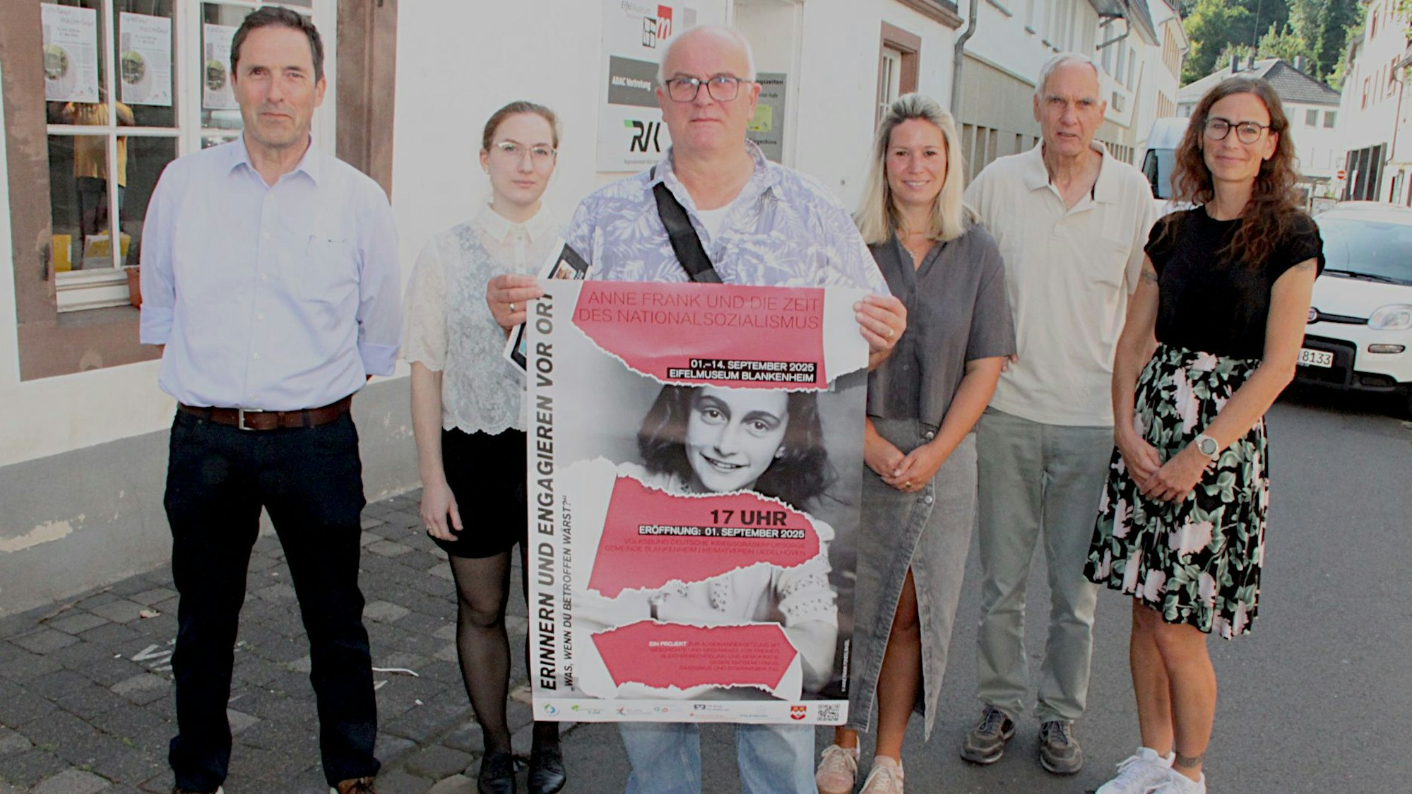 Drei Frauen und drei Männer, von denen einer ein Plakat hält, stehen vor dem Museum.