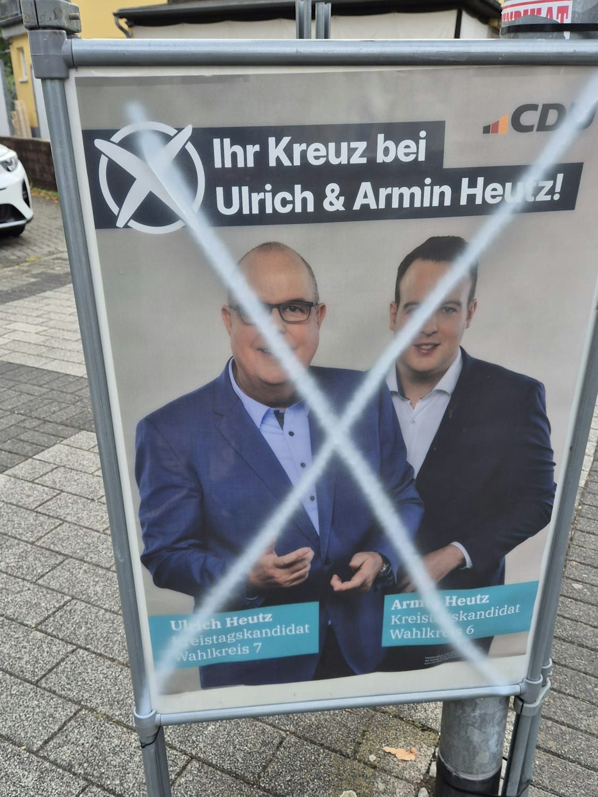 Ein Wahlplakat an einem Dreiecksständer an einem Laternenpfahl ist mit weißer Farbe beschmiert.