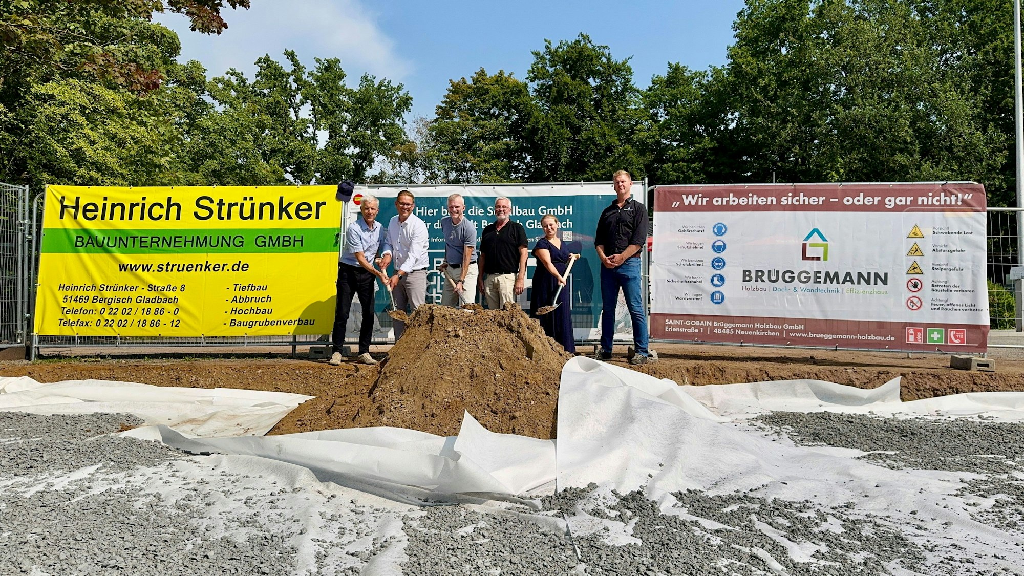Fünf Männer und eine Frau schippen Sand auf einen Haufen.