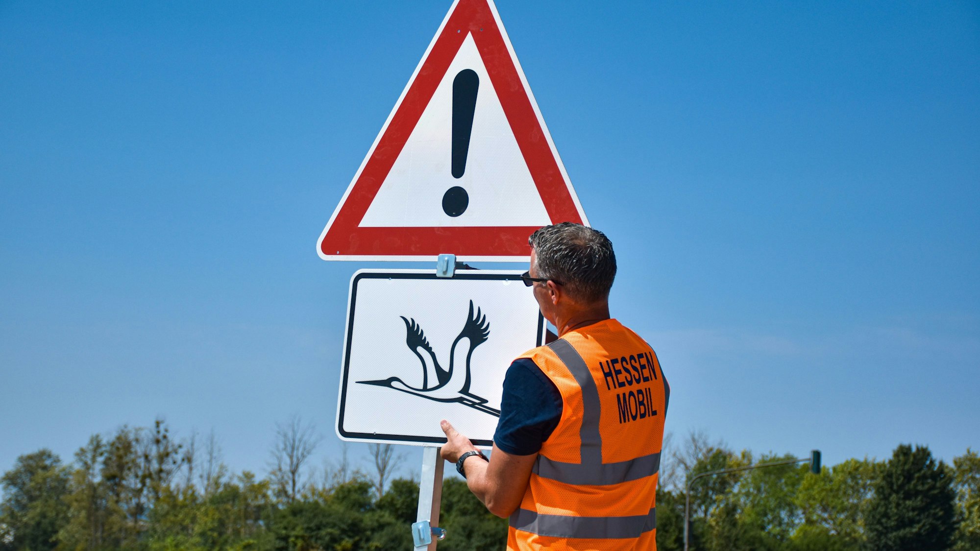 Ein Warnschild vor tieffliegenden Störchen wird in Wabern im Schwalm-Eder-Kreis montiert.