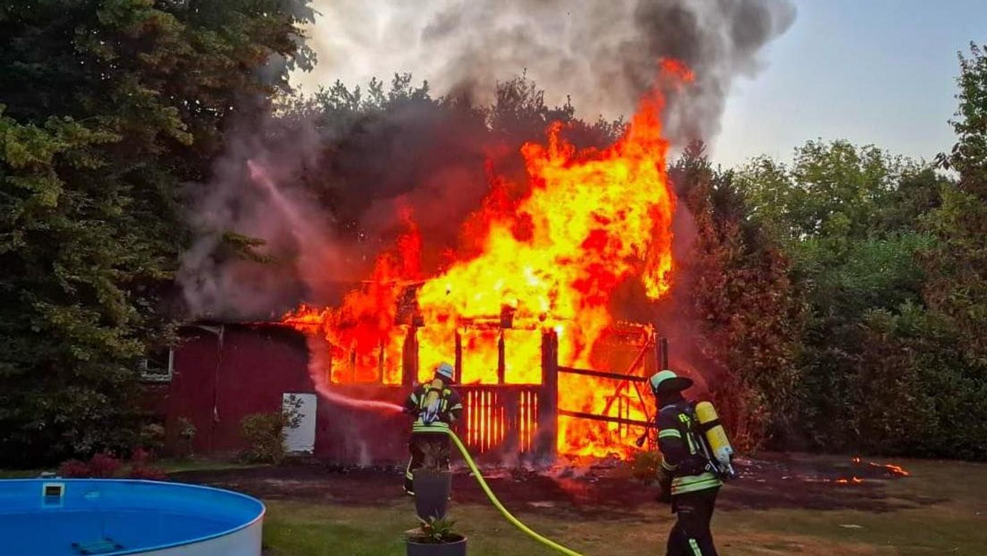 Ein Gartenhaus brennt lichterloh. Im Vordergrund Feuerwehrleute im Einsatz.