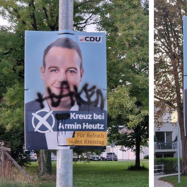 Zwei Plakate, die mit Farbe beschmiert worden sind, hängen an Laternenmasten in Bergisch Gladbach-Refrath.