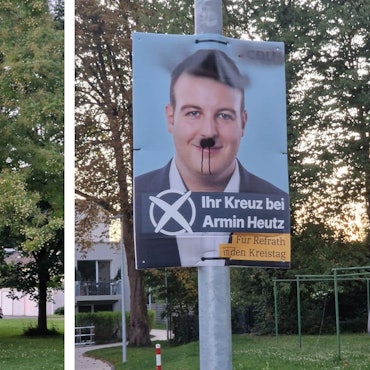 Zwei Plakate, die mit Farbe beschmiert worden sind, hängen an Laternenmasten in Bergisch Gladbach-Refrath.