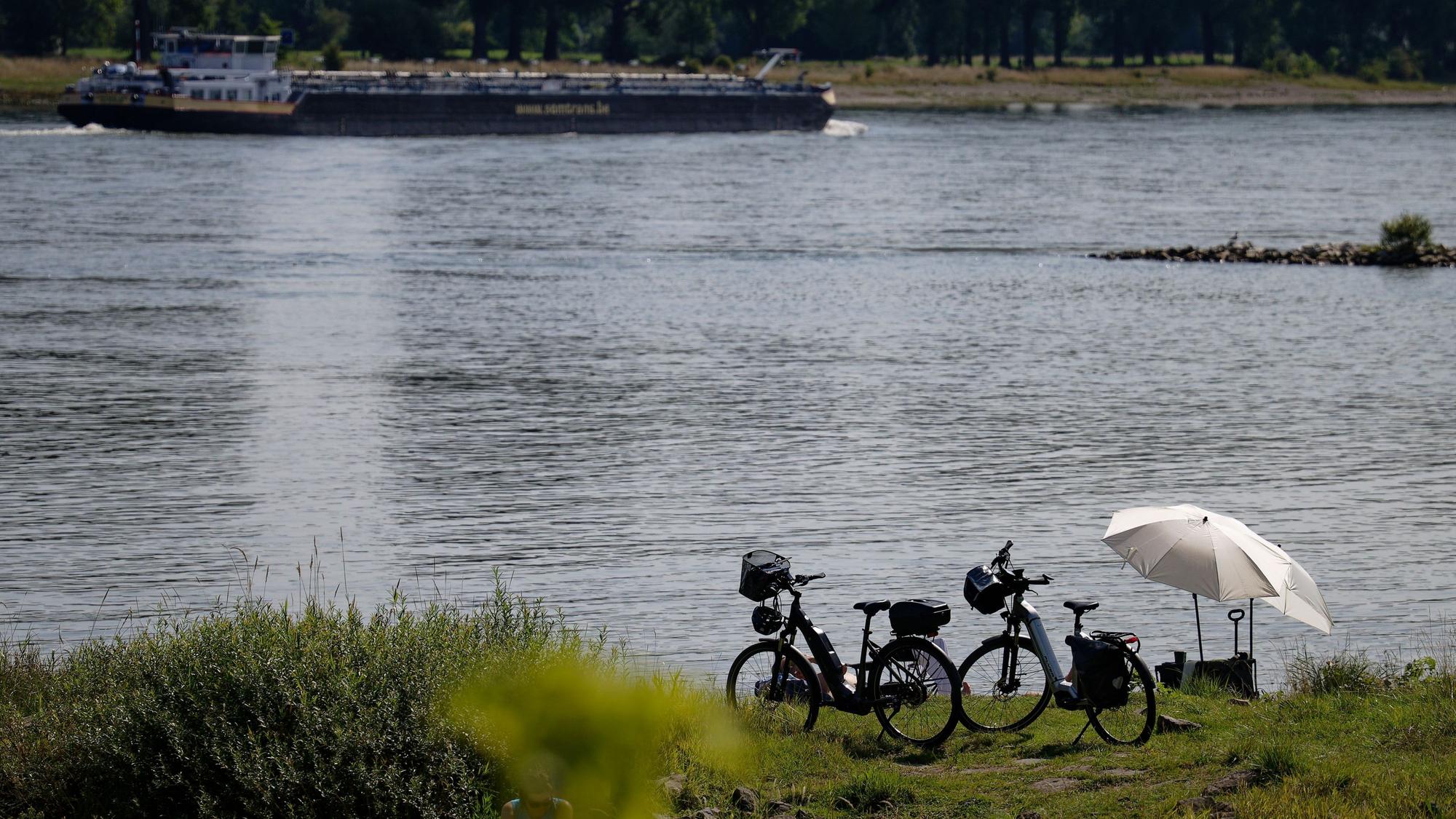 10.08.2025, Nordrhein-Westfalen, Köln: Fahrräder und Sonnenschirme stehen am Rheinufer bei Köln-Langel. Foto: Henning Kaiser/dpa +++ dpa-Bildfunk +++