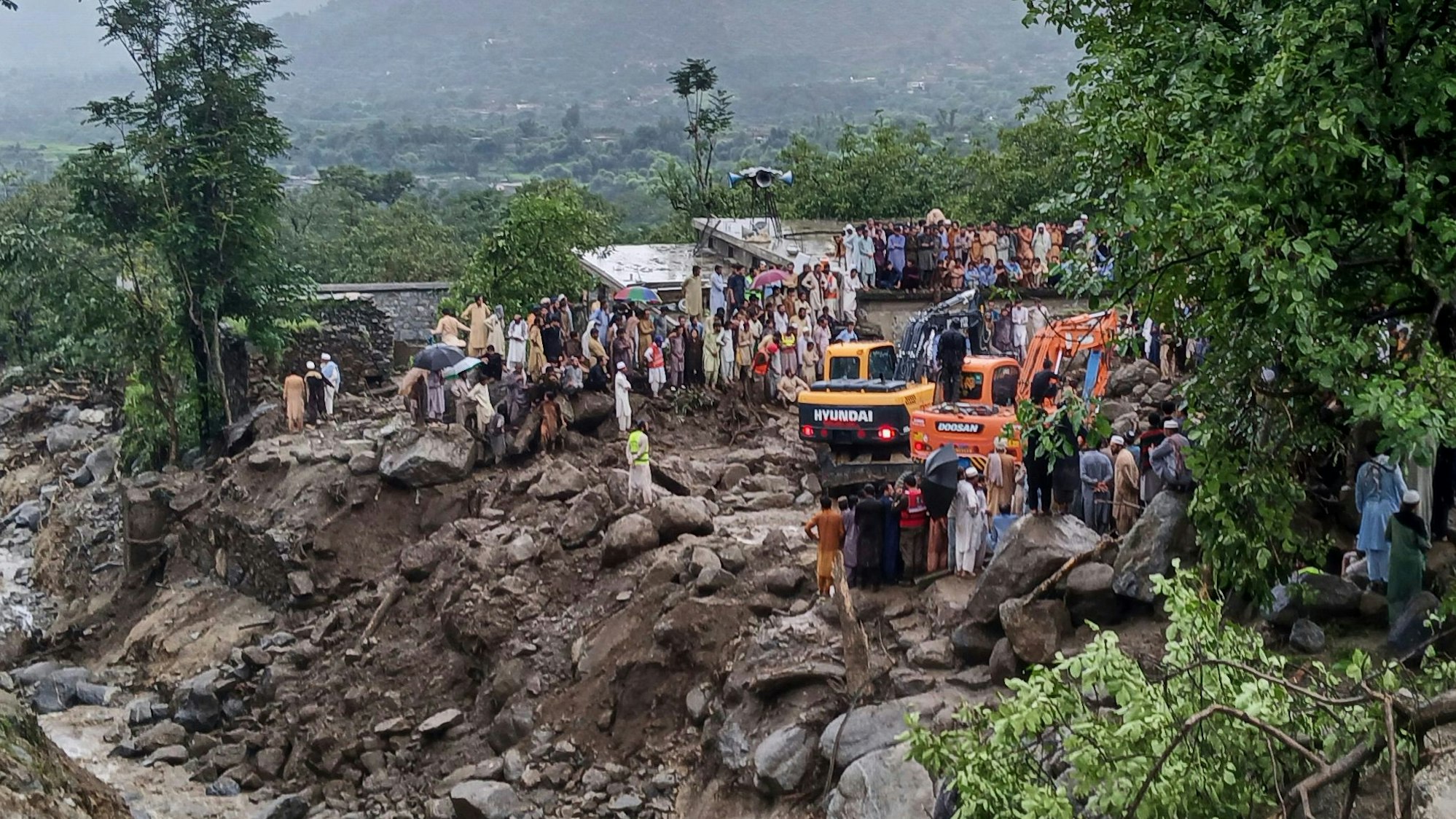 Rettungskräfte und Anwohner bergen mit schwerem Gerät Menschen zwischen großen Steinen.