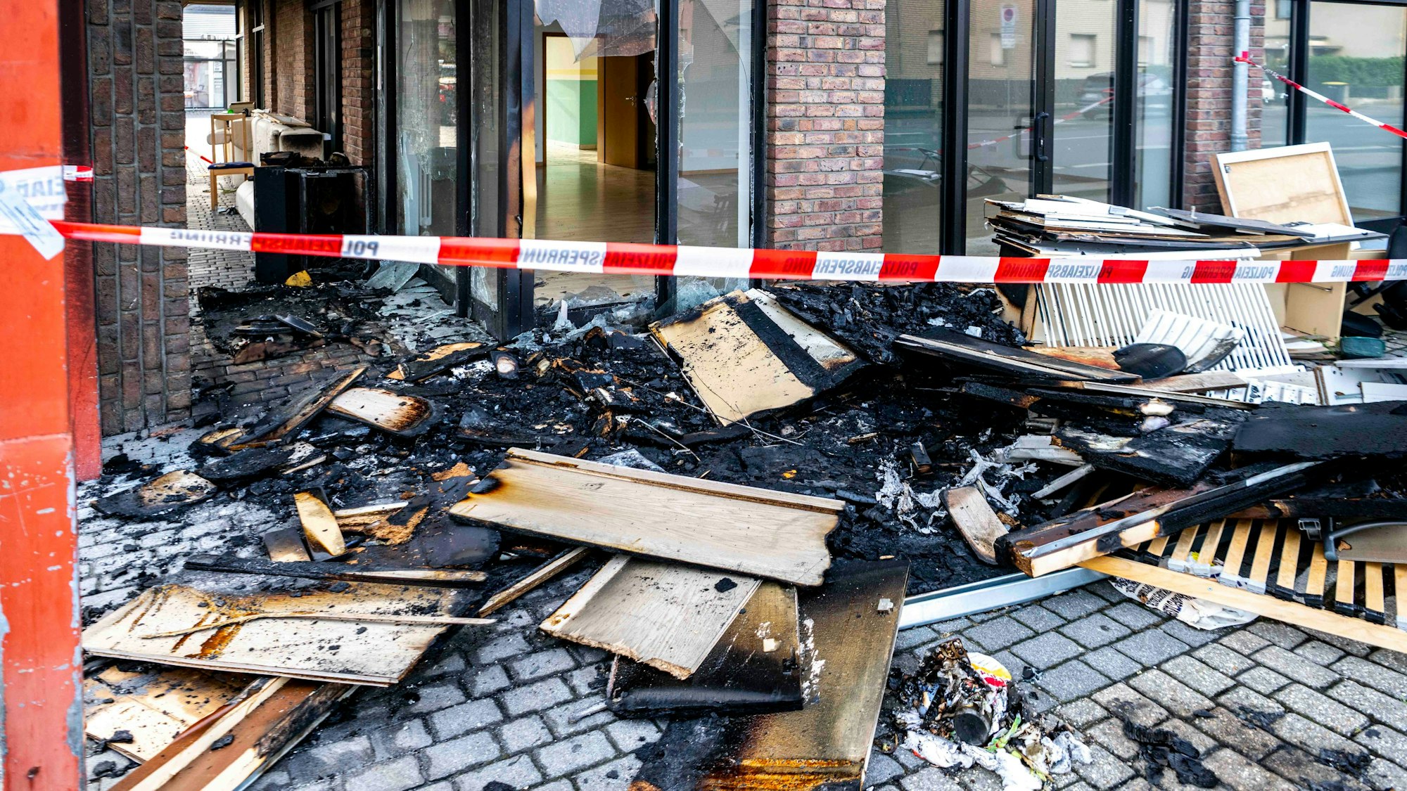 Das Bild zeigt den von der Polizei beschlagnahmten Bereich am Gebäude. Es ist noch verkohlter Sperrmüll zu erkennen.