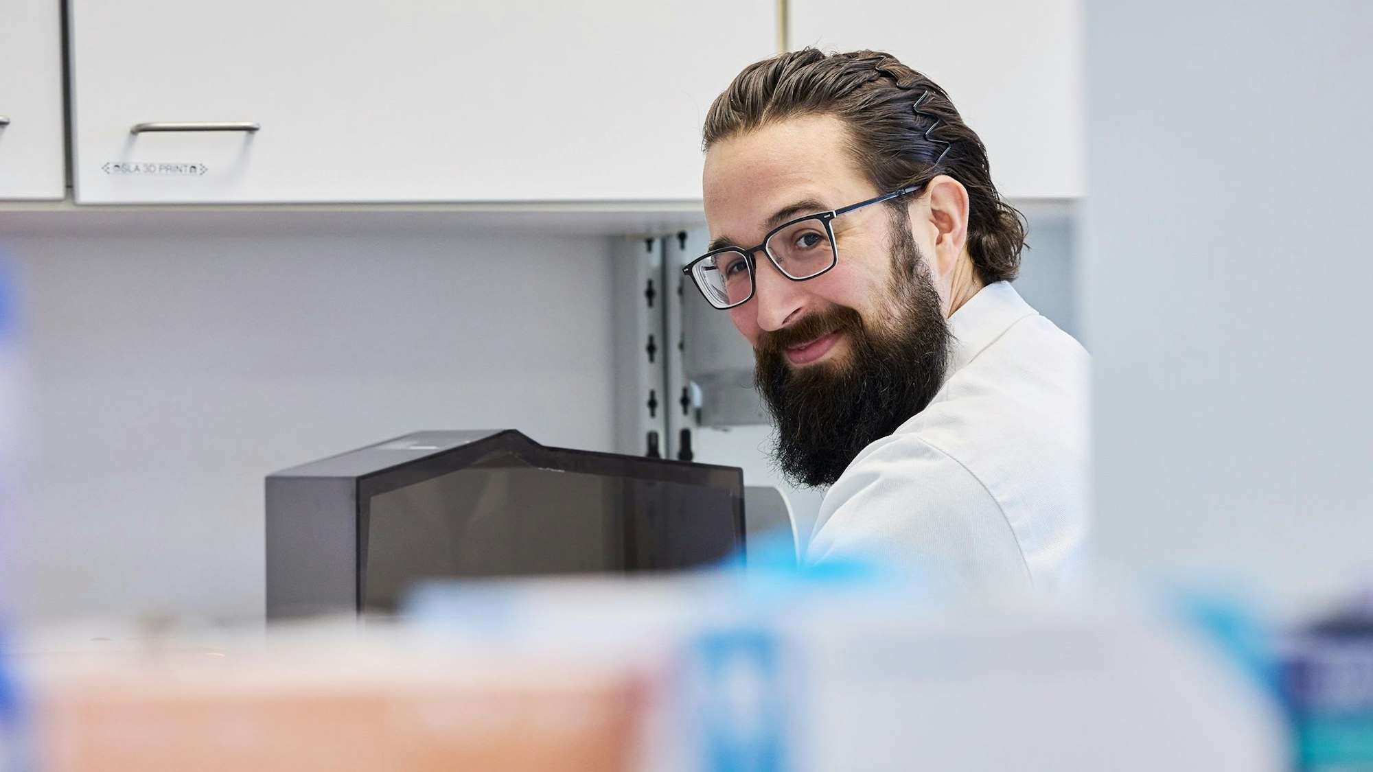 Robin Bayer sitzt im Arztkittel im Labor.