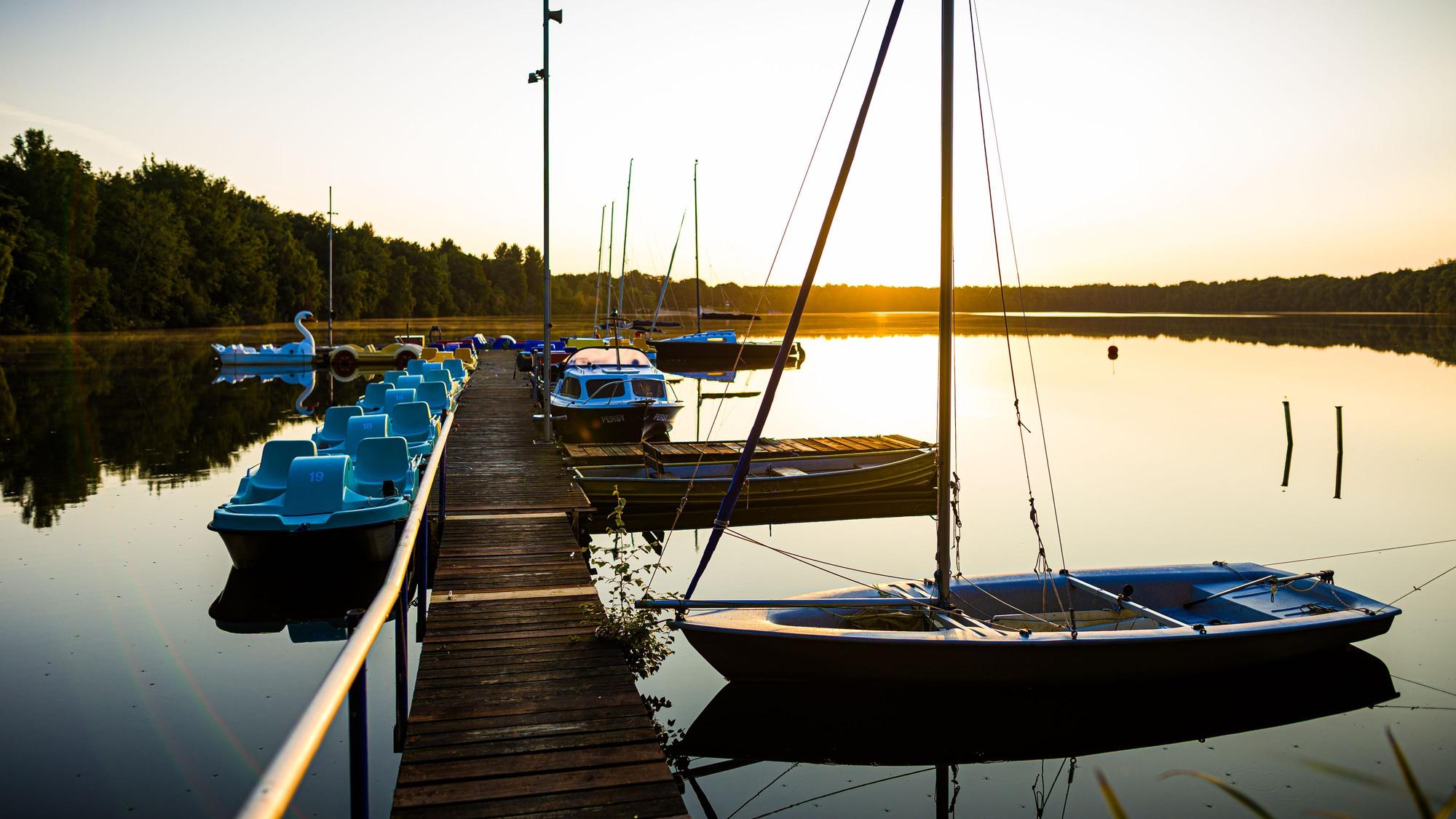 Kleine Boote liegen im Licht der aufgehenden Sonne an einem Steg im See.