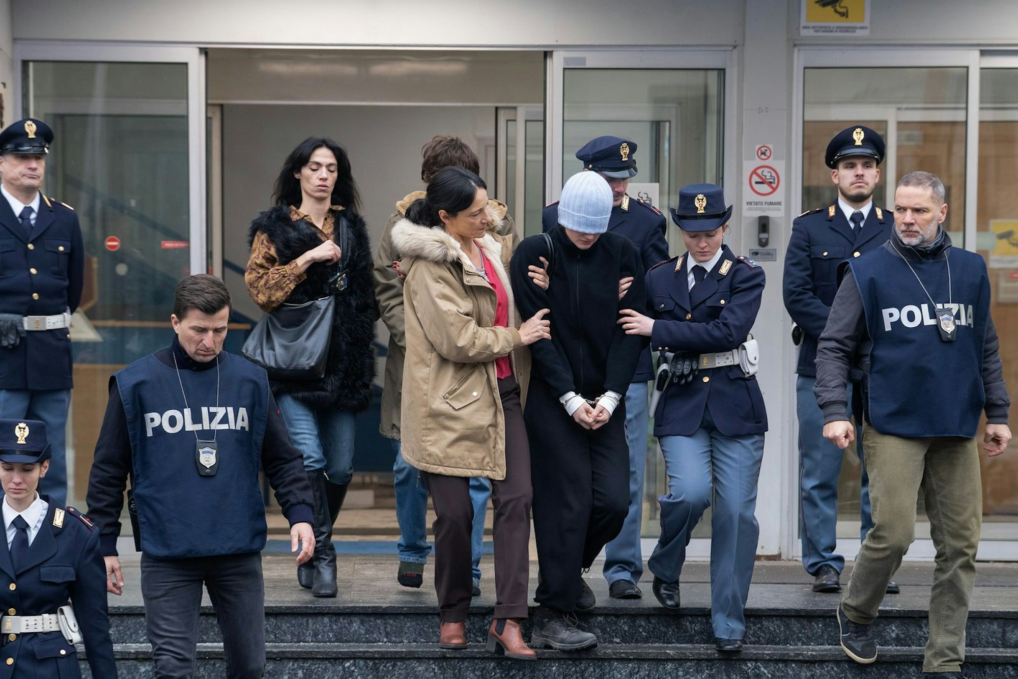Amanda Knox (Grace van Patten) wird verdeckt durch eine tief ins Gesicht gezogene Mütze aus einem italienischen Gerichtsgebäude geführt. Der Prozess gegen sie ist längst zu einem international viel beachteten Medienspektakel geworden. (Bild: Disney/Adrienn Szabo)