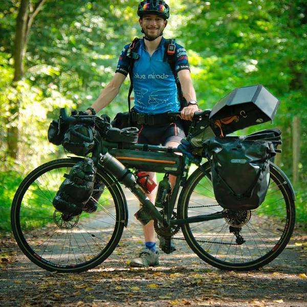 Florian Berg steht in Fahrradkleidung hinter seinem vollgepackten Reiserad.
