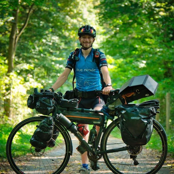 Florian Berg steht in Fahrradkleidung hinter seinem vollgepackten Reiserad.