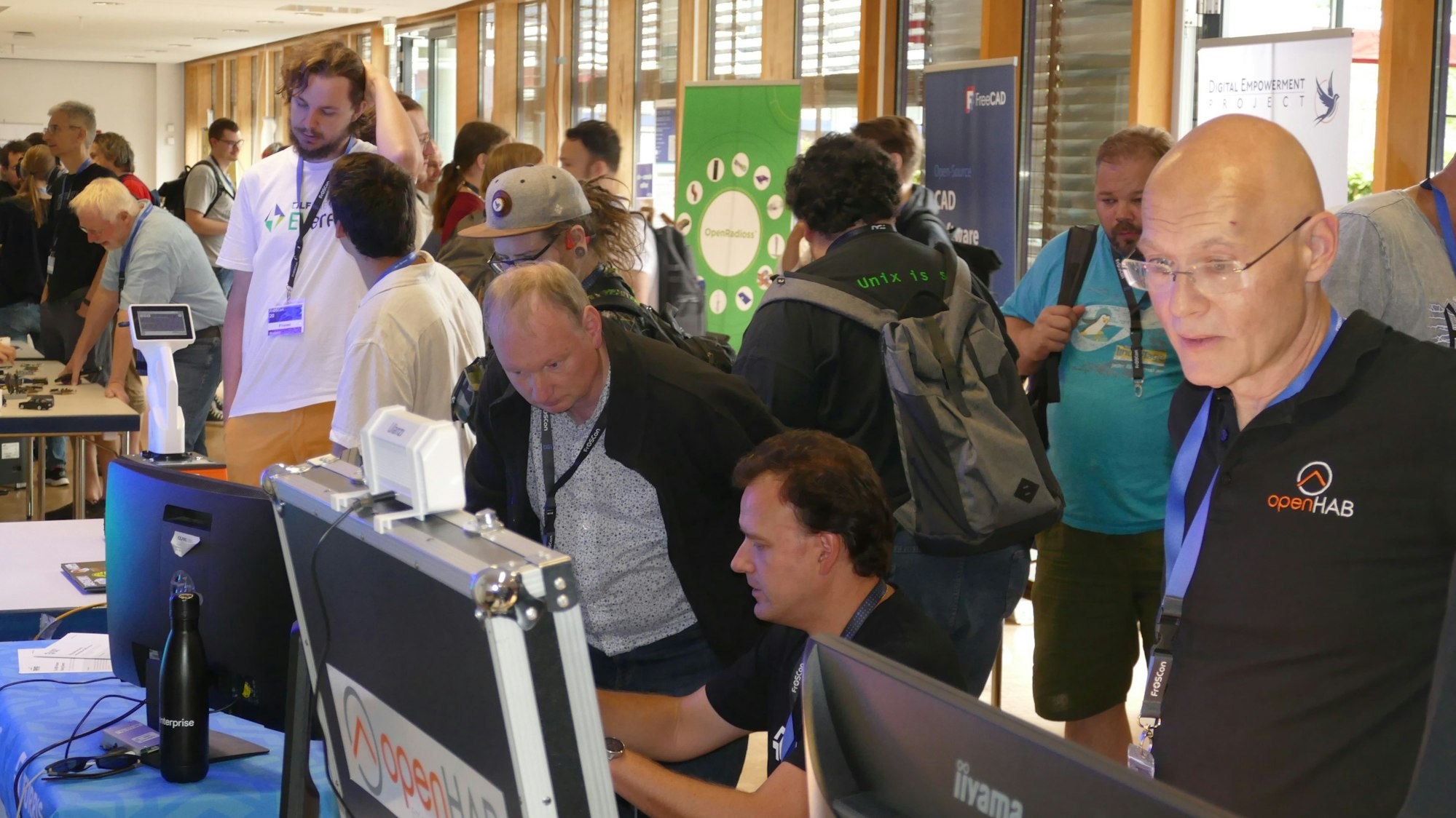 Besucher einer Messe diskutieren vor Computerbildschirmen.