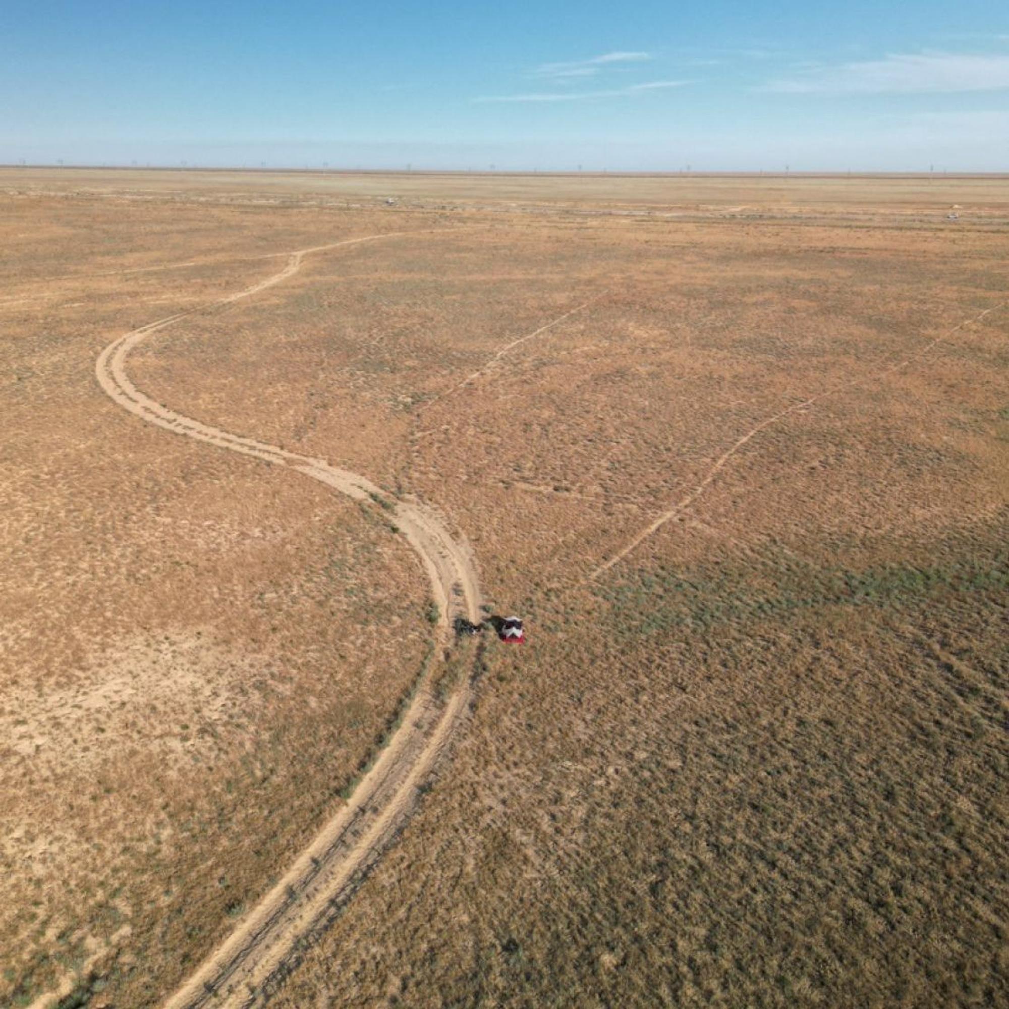 Eine Luftaufnahme zeigt eine Sandpiste, die durch eine Wüstenlandschaft führt. Am Wegesrand ist ein kleines Zelt zu erkennen.