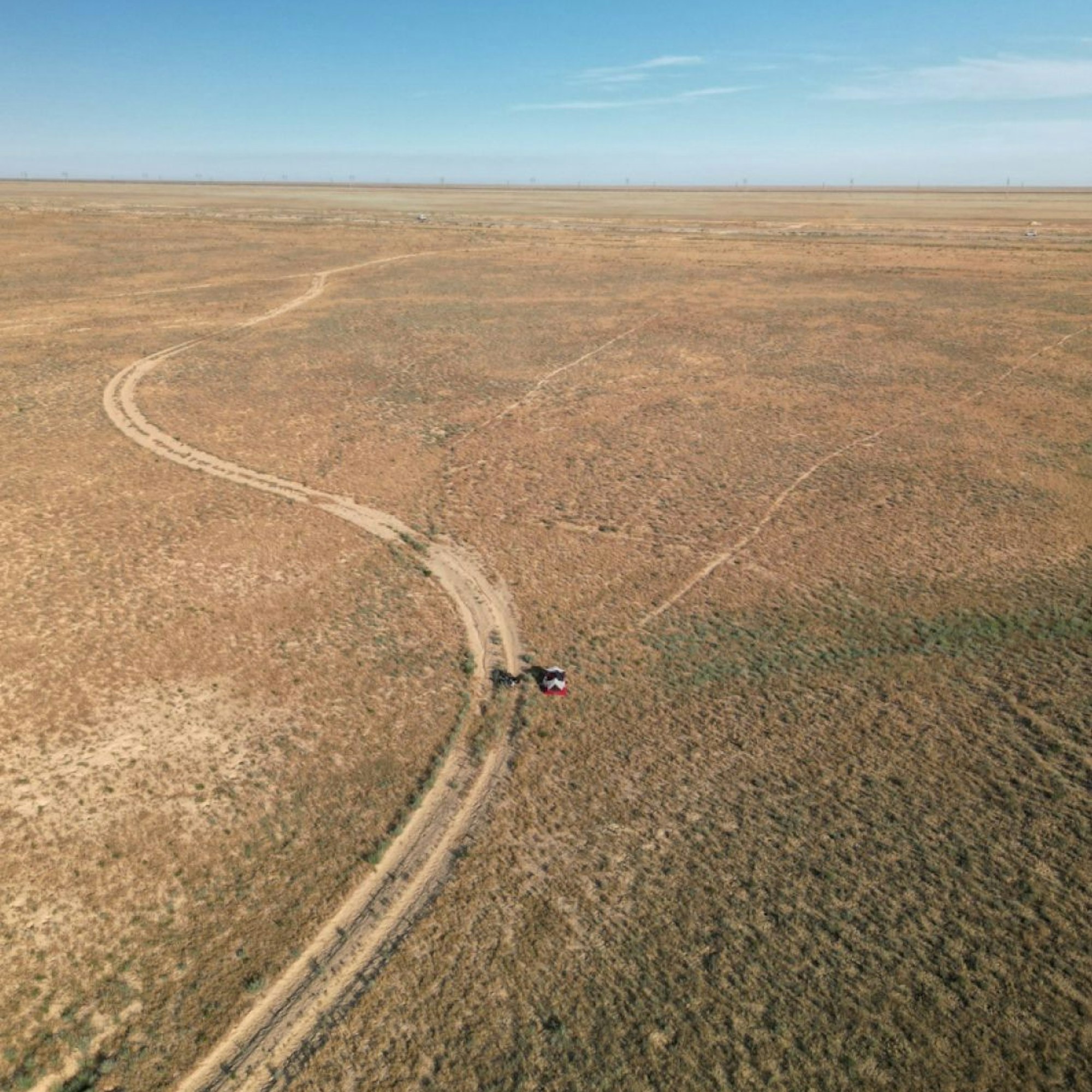 Eine Luftaufnahme zeigt eine Sandpiste, die durch eine Wüstenlandschaft führt. Am Wegesrand ist ein kleines Zelt zu erkennen.