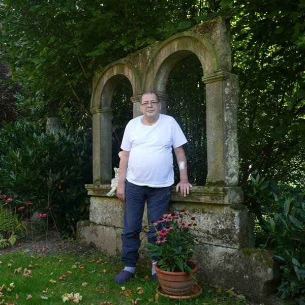 Ein Mann im weißen T-Shirt steht in einem Garten.
