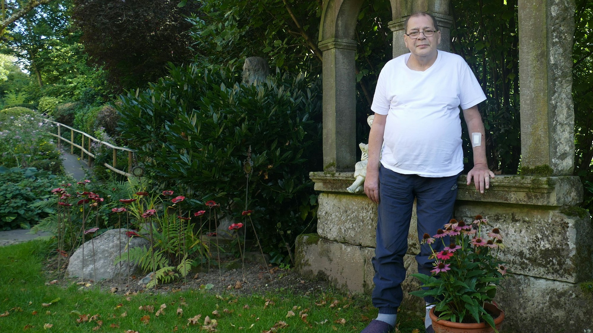 Ein Mann im weißen T-Shirt steht in einem Garten.