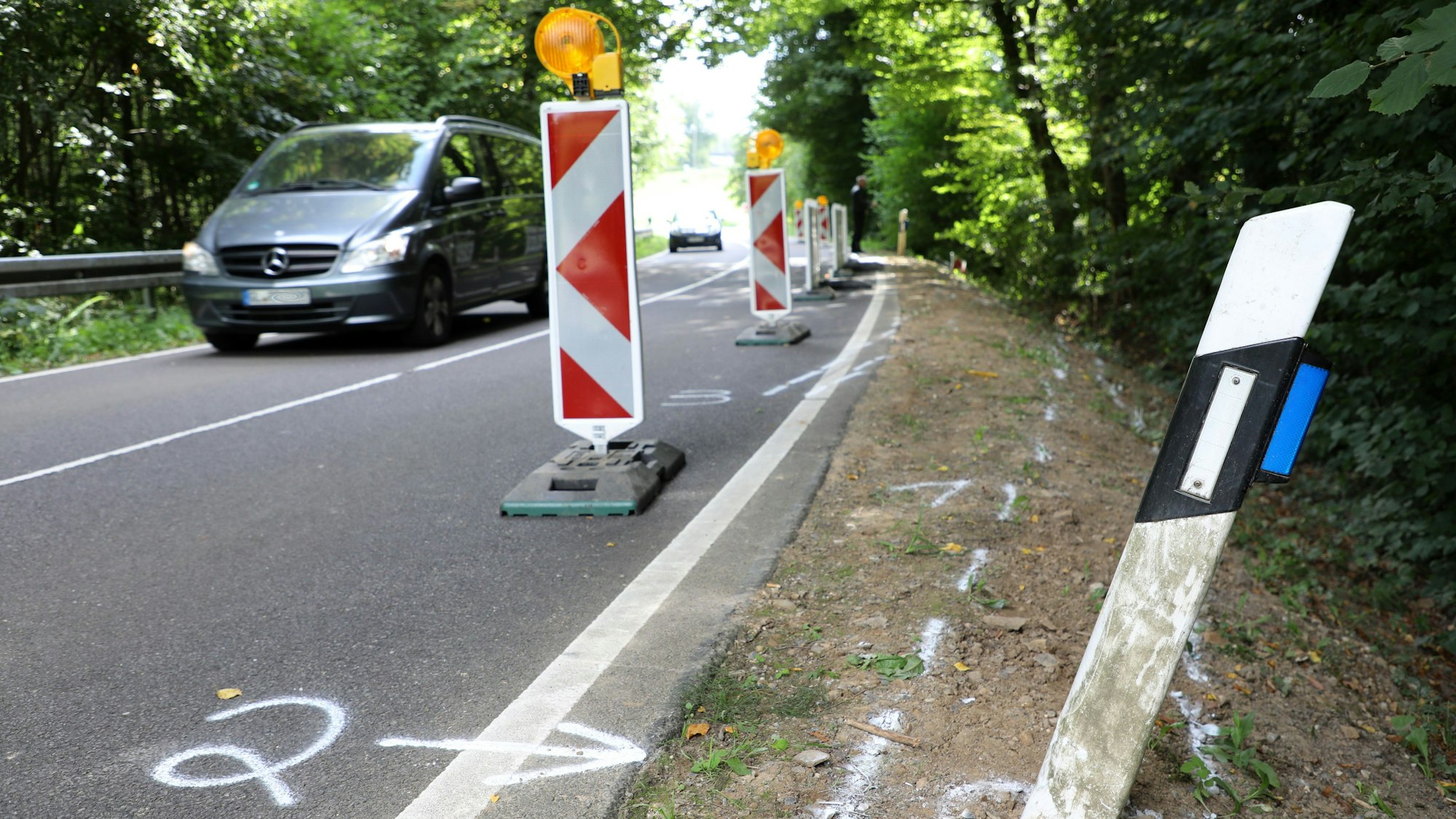 Auf einer Straße im Dürschtal bei Kürten-Dürscheid stehen Warnbaken, auf dem Boden sind Sprühkreidemarkierungen von einem Unfall zu sehen.