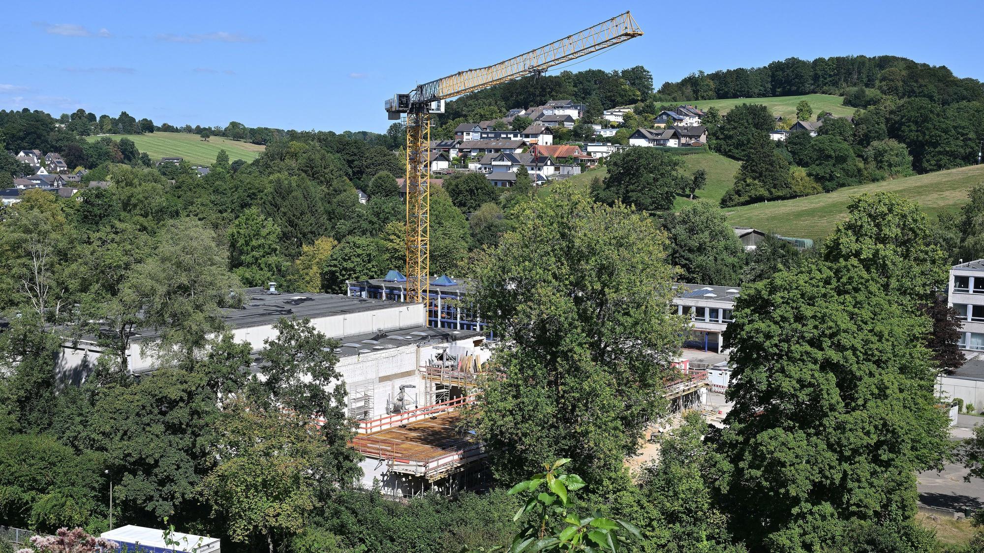 Ein großer Kran steht über unfertigen Rohbauten in einem grünen Tal.