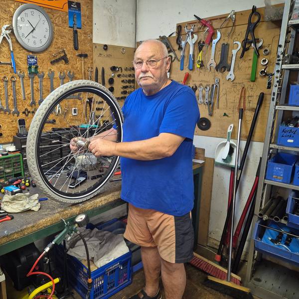 Ein Mann steht in der Werkstatt seines Fahrradgeschäfts und hält einen Reifen in den Händen.