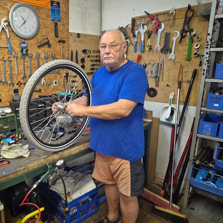 Ein Mann steht in der Werkstatt seines Fahrradgeschäfts und hält einen Reifen in den Händen.