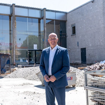 Das Foto zeigt Landrat Frank Rock auf der Baustelle vor der Glasfassade am Eingang des Berufskollegs.