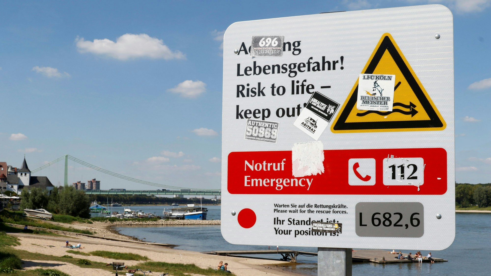 Am Rodenkirchener Rheinufer steht ein Hinweisschild mit der Aufschrift "Achtung Lebensgefahr", das vor Schwimmen im Rhein warnt.