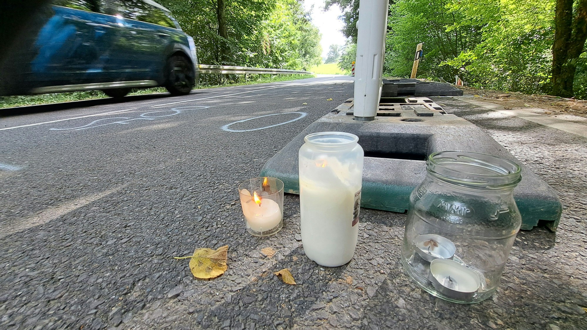 Kerzen stehen zwischen Warnbaken auf dem Asphalt der Dürschtalstraße bei Kürten-Dürscheid.