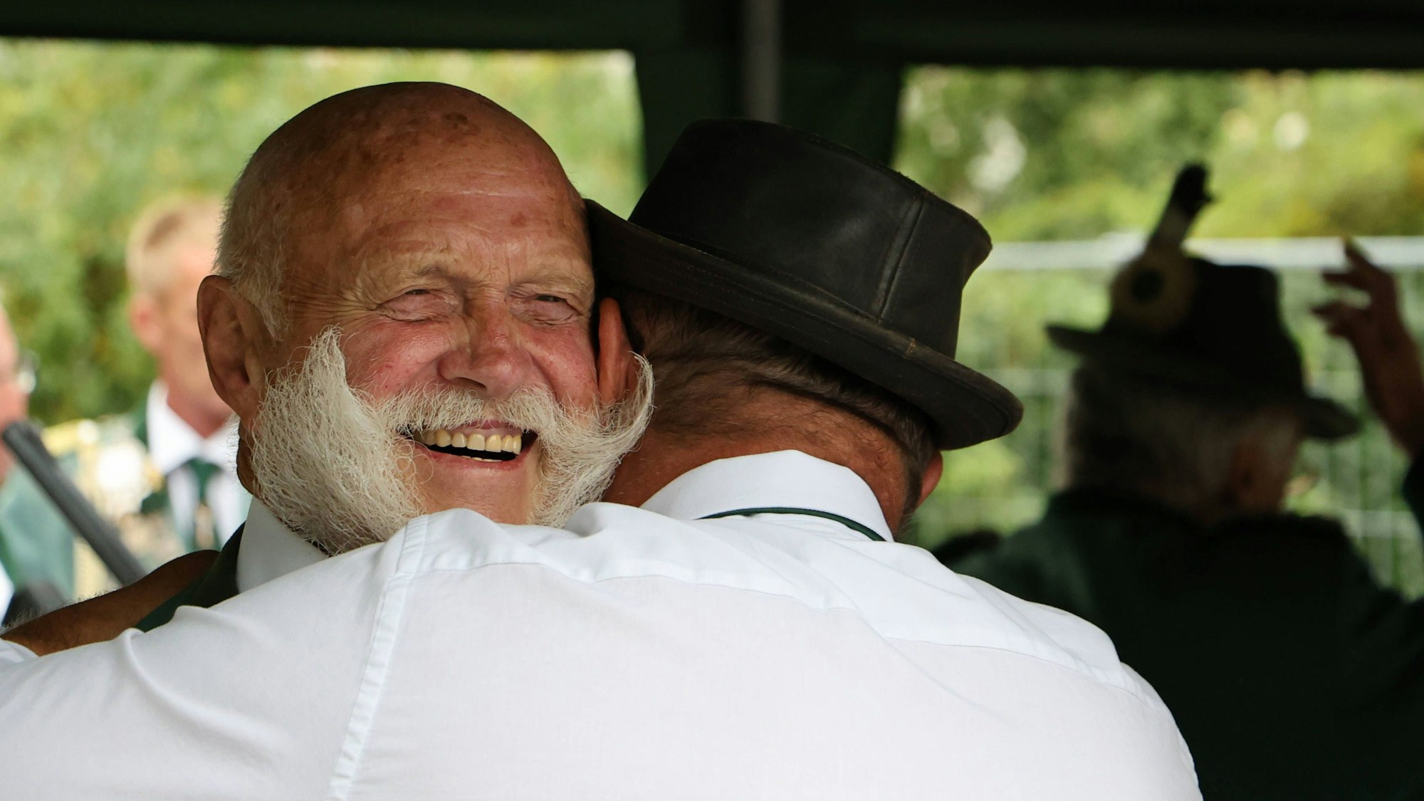 Ernst Pingen freut sich, während er einen anderen Herren umarmt, der einen Hut trägt.