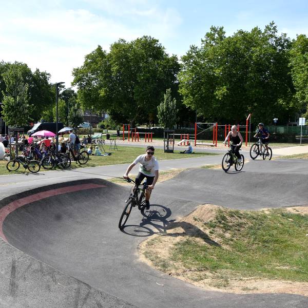Jugendliche fahren auf ihren Mountainbikes auf der Strecke, im Hintergrund haben viele auf einer Wiese Platz genommen, um auf einer großen Leinwand den Film zu sehen
