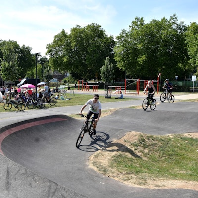 Jugendliche fahren auf ihren Mountainbikes auf der Strecke, im Hintergrund haben viele auf einer Wiese Platz genommen, um auf einer großen Leinwand den Film zu sehen