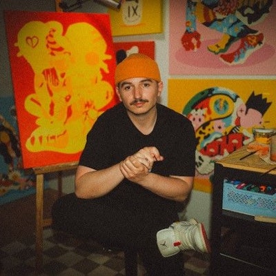 Der Künstler sitzt in seinem Atelier vor seinen Werken.