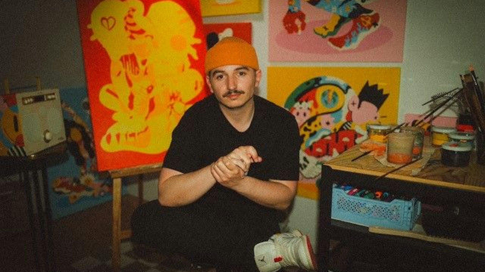 Der Künstler sitzt in seinem Atelier vor seinen Werken.