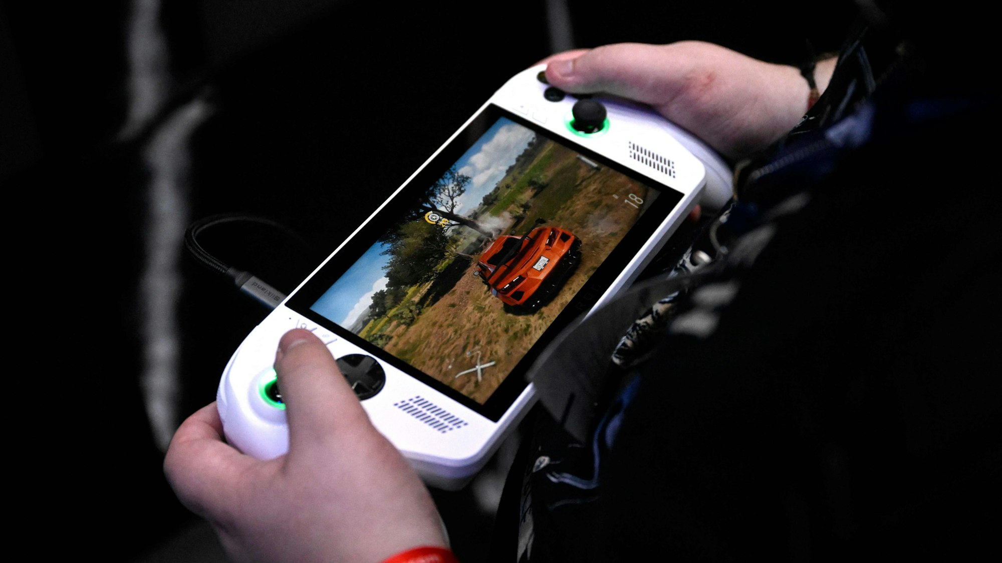 Ein Gamescom-Besucher spielt auf einer Mini-Konsole. Auf dem Bildschirm ist ein rotes Rennauto zu sehen.