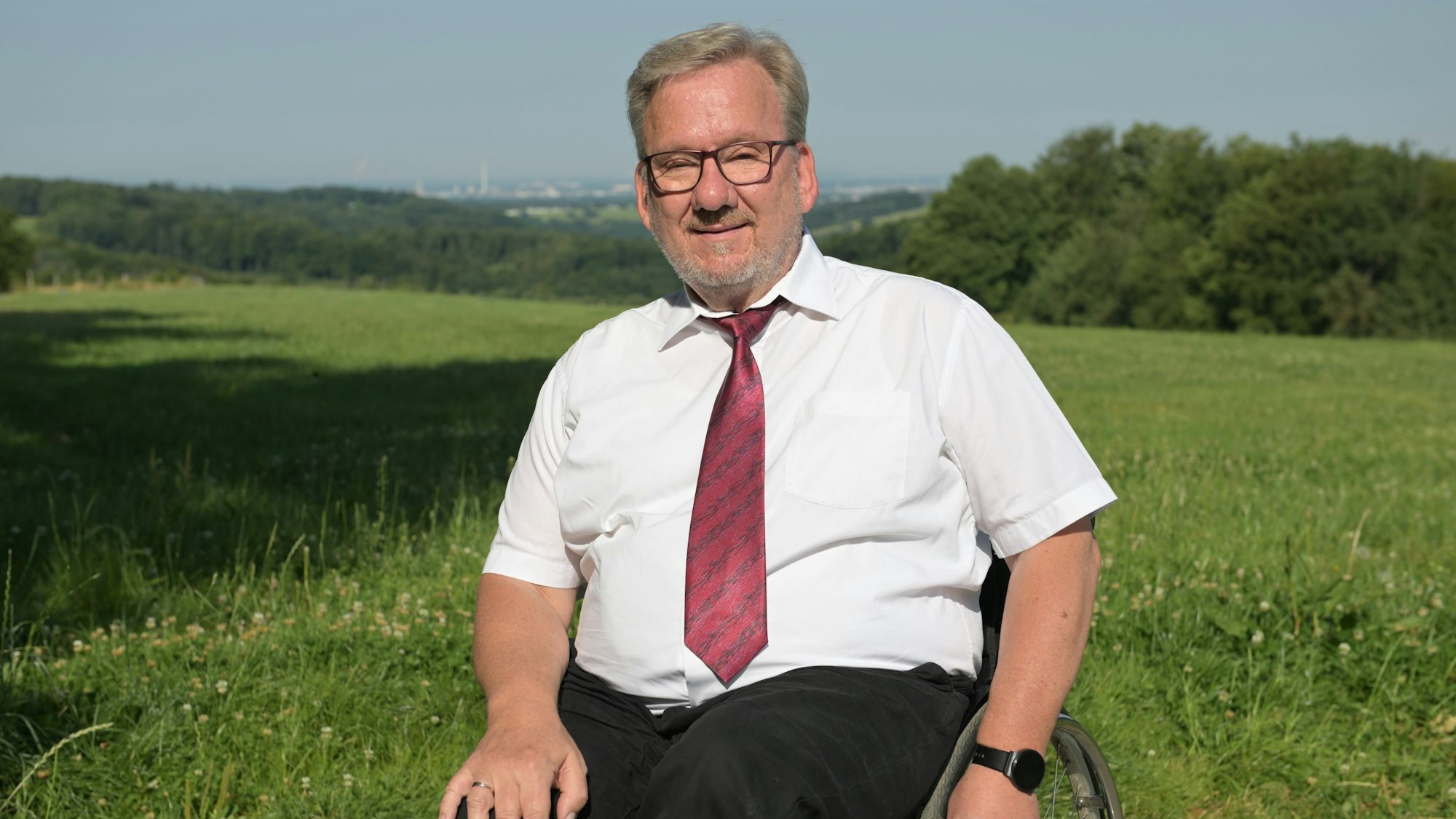 Ein Mann im Rollstuhl vor einer grünen Wiese, dahinter die Silhouette von Leverkusen.
