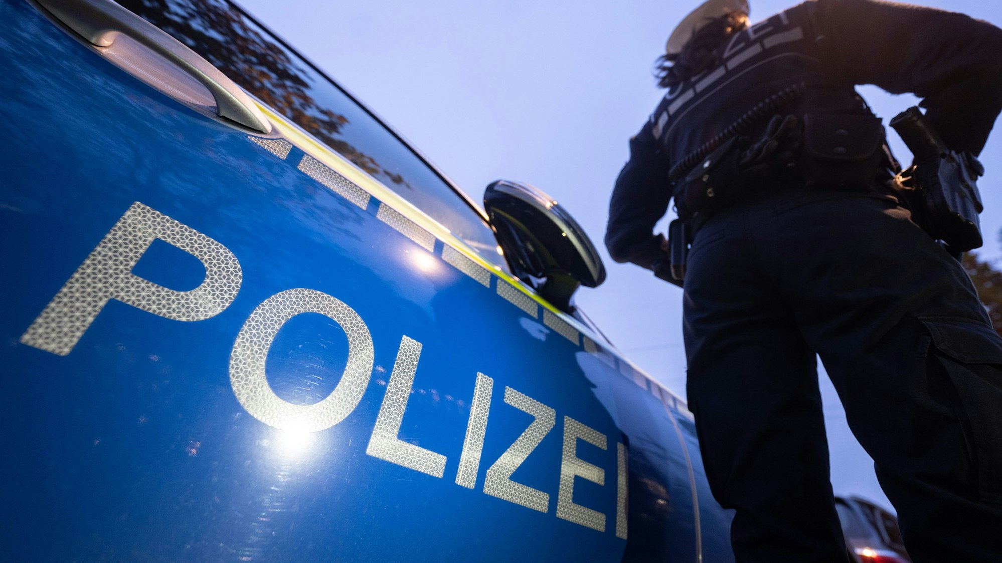 Eine Polizistin steht neben einem Polizeifahrzeug.