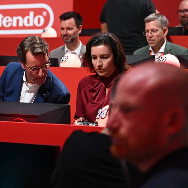 NRW-Ministerpräsident Hendrik Wüst (CDU) sitzt am Gamescom-Messestand von Nintendo neben der für Games zuständigen Bundesforschungsministerin Dorothee Bär (CSU) und macht sich bereit für das Konsolen-Rennspiel Partie Mario Kart.