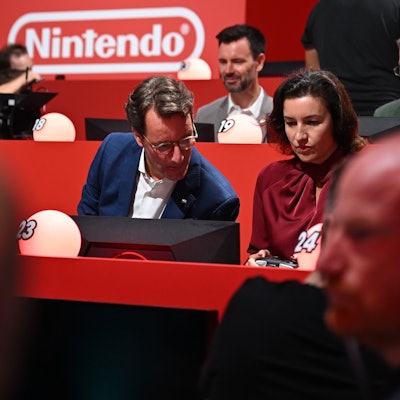 NRW-Ministerpräsident Hendrik Wüst (CDU) sitzt am Gamescom-Messestand von Nintendo neben der für Games zuständigen Bundesforschungsministerin Dorothee Bär (CSU) und macht sich bereit für das Konsolen-Rennspiel Partie Mario Kart.