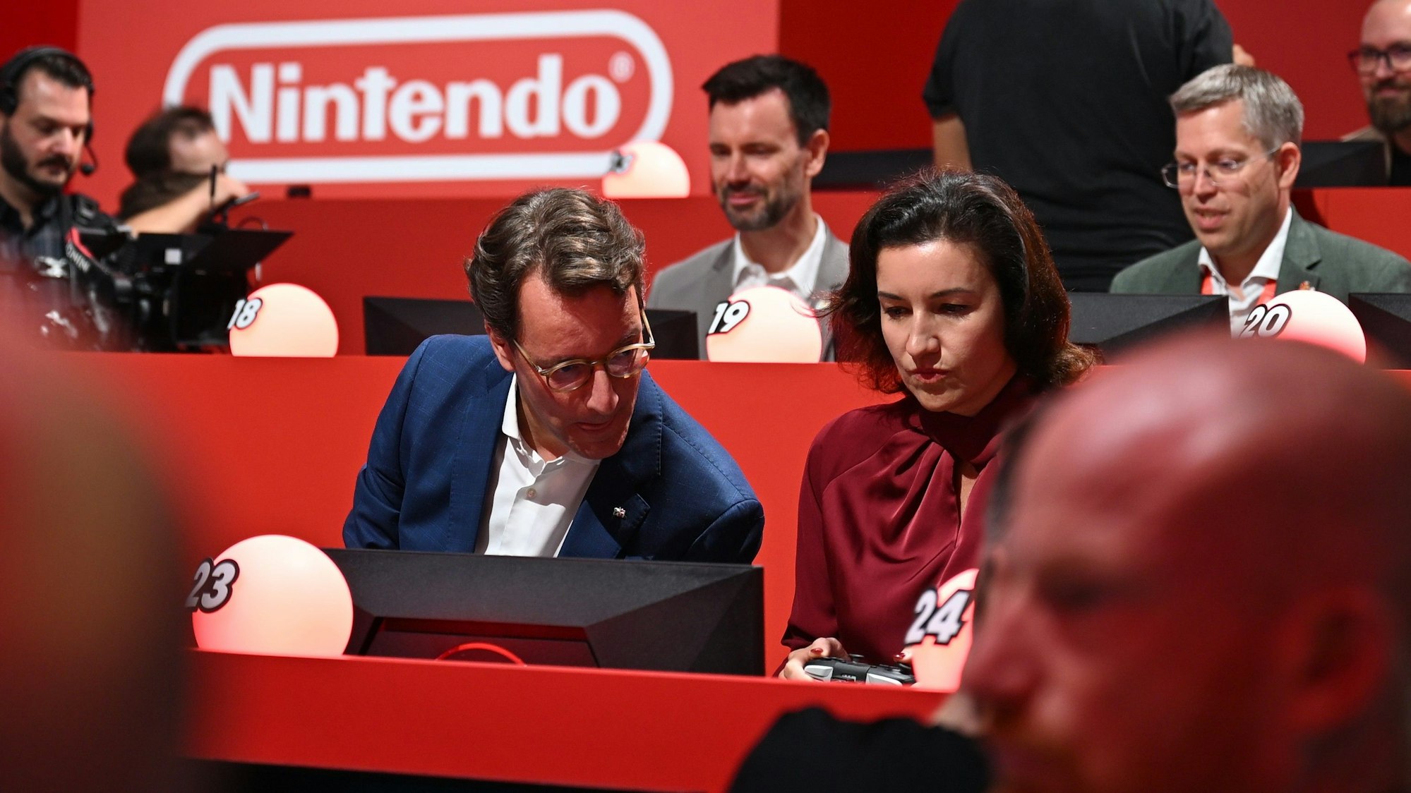 NRW-Ministerpräsident Hendrik Wüst (CDU) sitzt am Gamescom-Messestand von Nintendo neben der für Games zuständigen Bundesforschungsministerin Dorothee Bär (CSU) und macht sich bereit für das Konsolen-Rennspiel Partie Mario Kart.