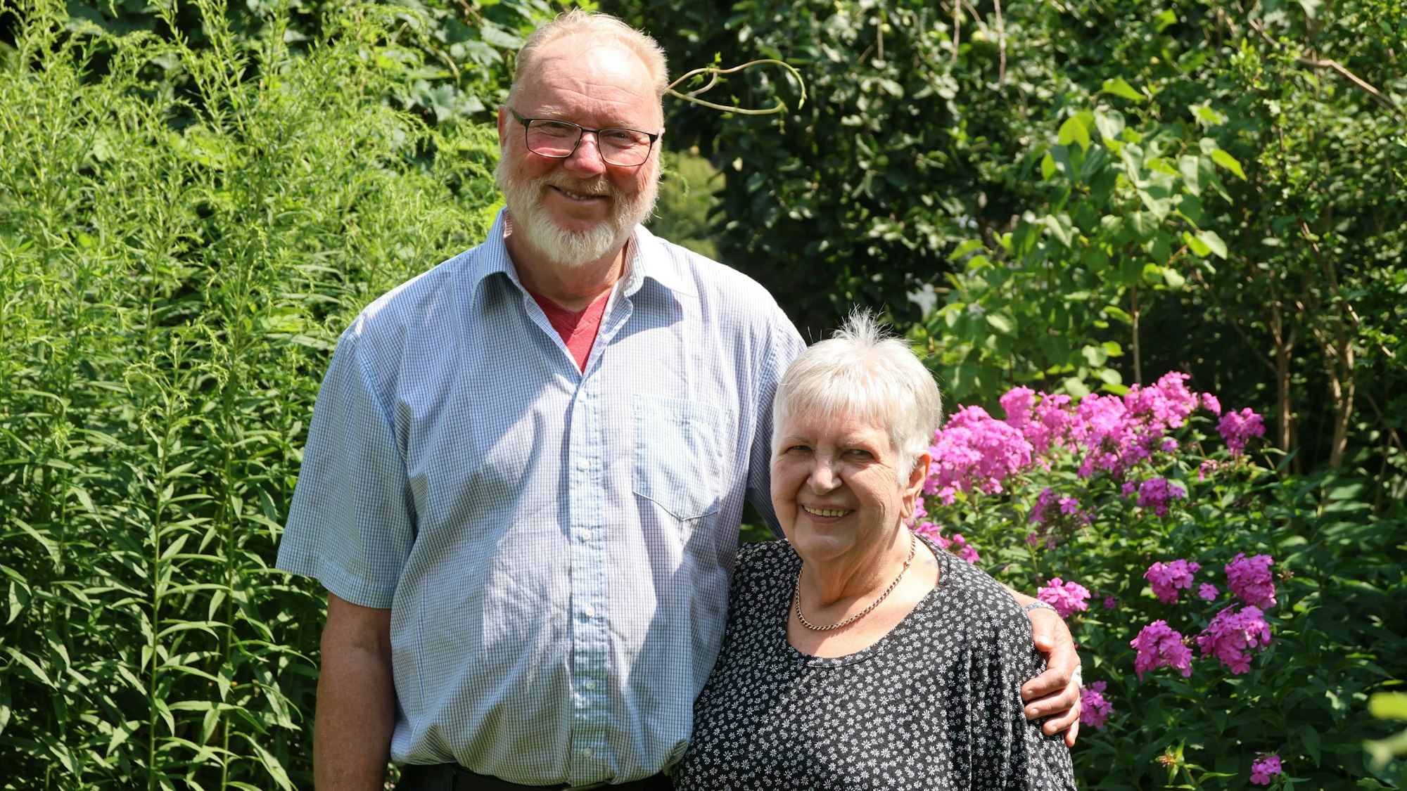 Ein Ehepaar steht im Arm liegend in einem Garten.