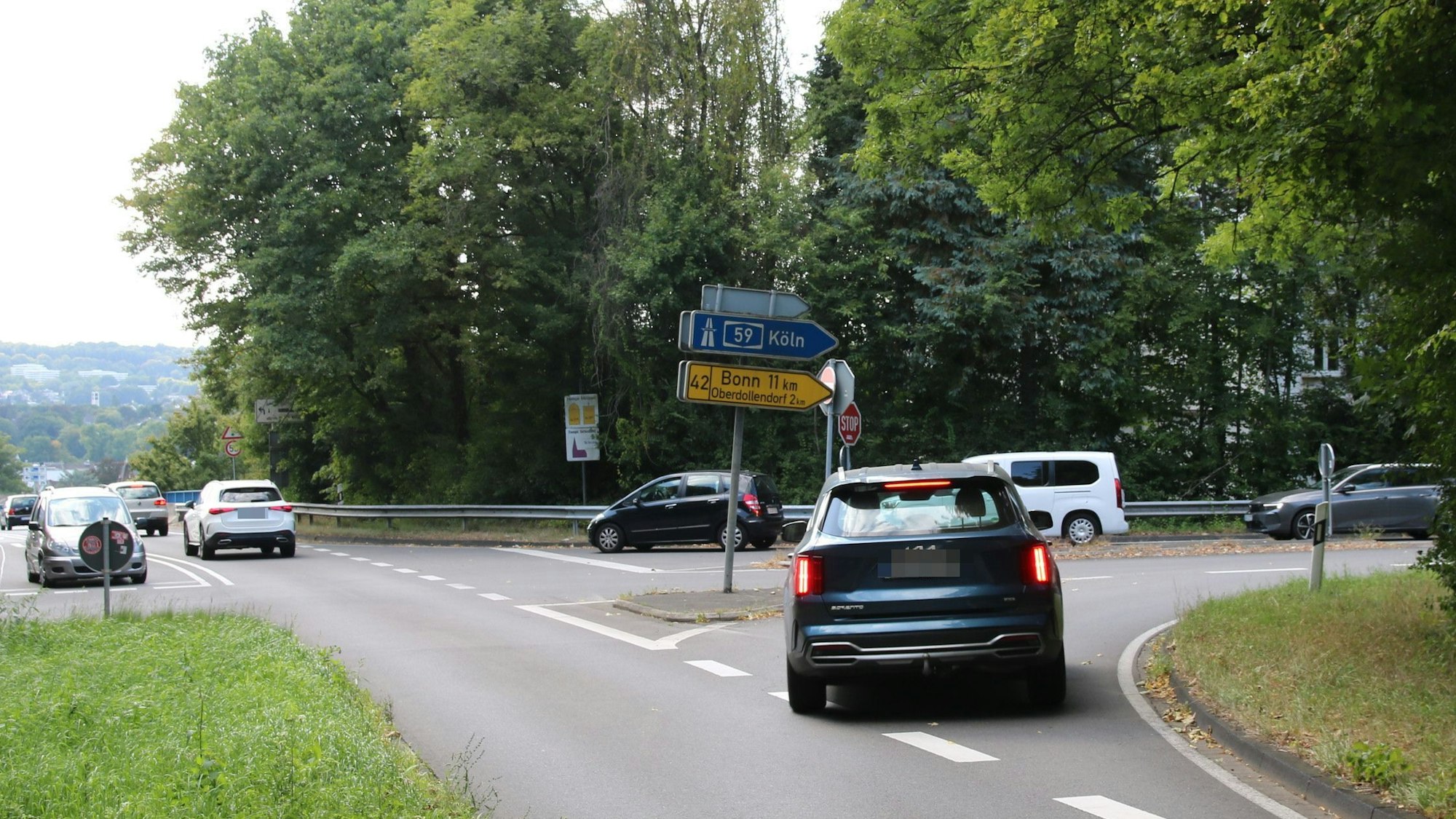Eine Straßenkreuzung mit mehreren Autos. Schilder weisen auf die B42 nach Bonn und die A59 nach Köln hin.