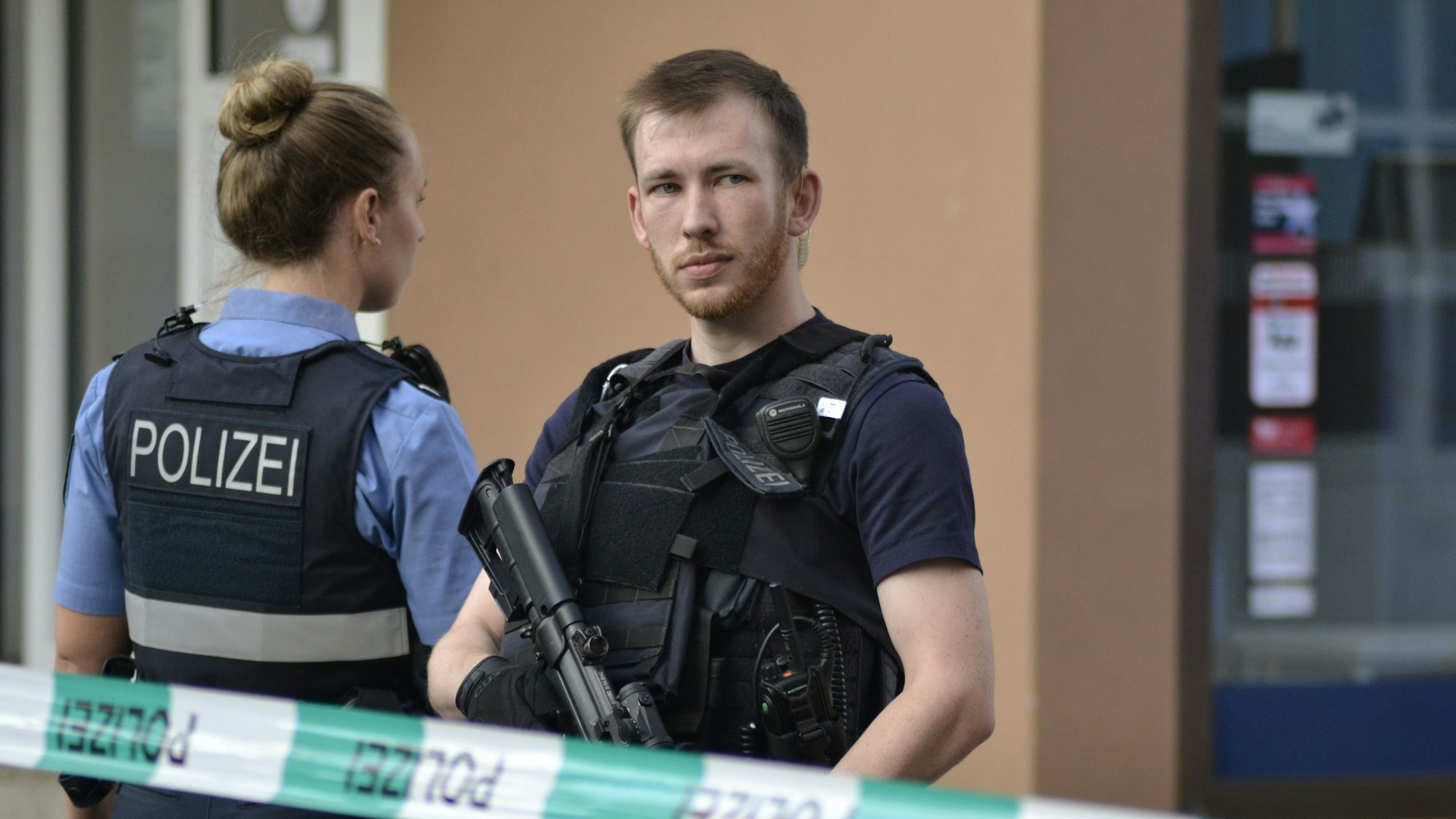 21.08.2025, Saarland, Völklingen: Ein Polizist steht mit einem Maschinengewehr am Tatort und sichert den Bereich. Nach einem Raubüberfall auf eine Tankstelle im saarländischen Völklingen ist ein Polizist durch Schüsse getötet worden. Nach Angaben der Polizei hatte der mutmaßliche Täter dem Beamten bei einem Gerangel die Dienstwaffe entrissen und geschossen. Foto: Gianni Gattus/dpa +++ dpa-Bildfunk +++