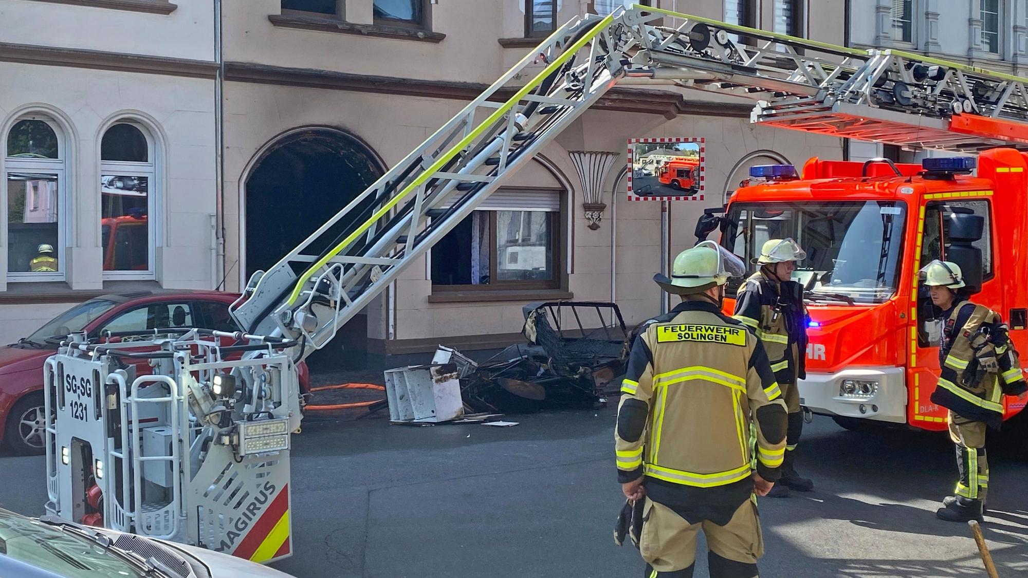 Feuerwehrleute stehen vor einem verrußten Hauseingang.