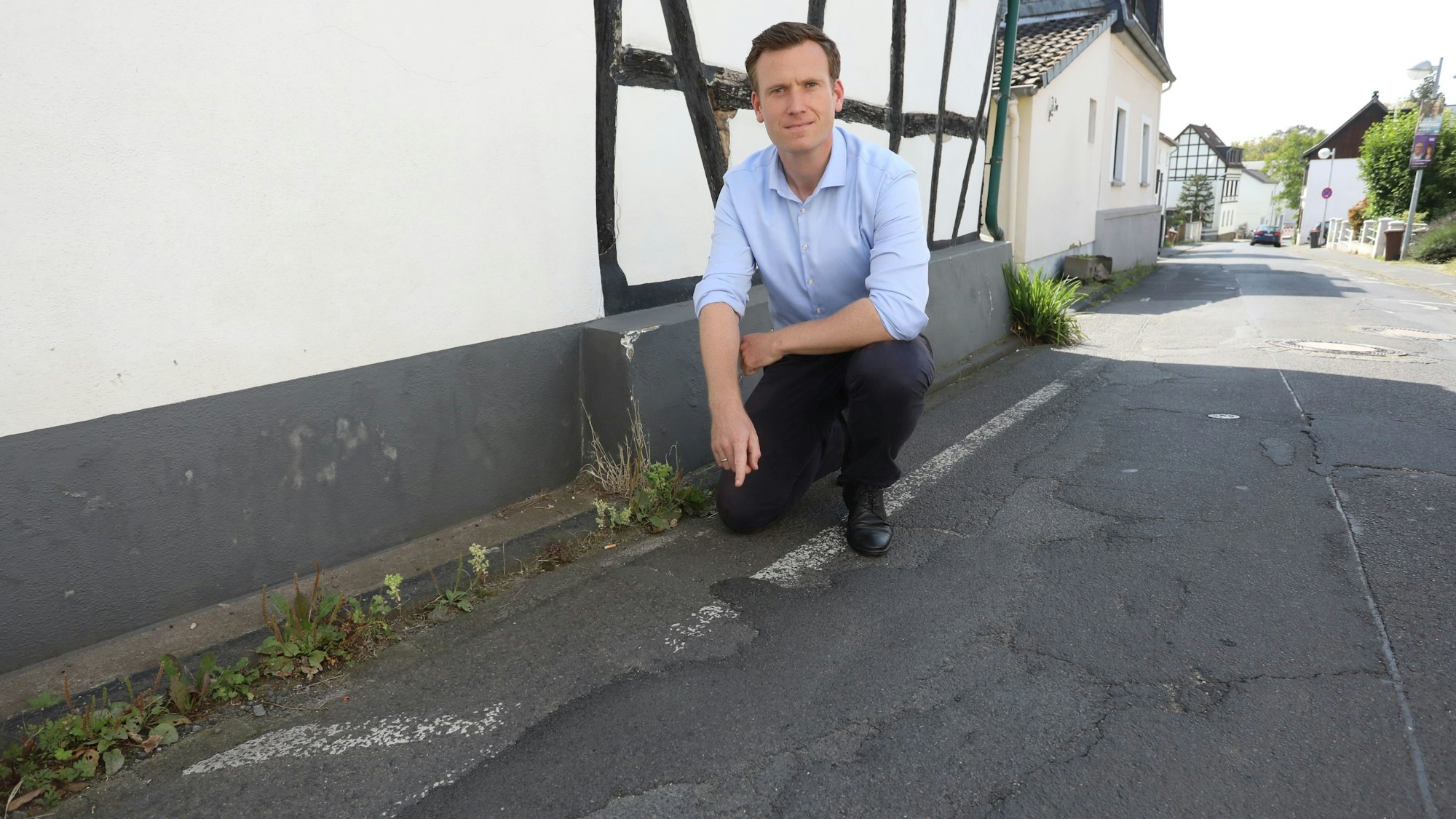 Ein Mann in blauem Hemd kniet am Rand einer Straße mit vielen Schlaglöchern.