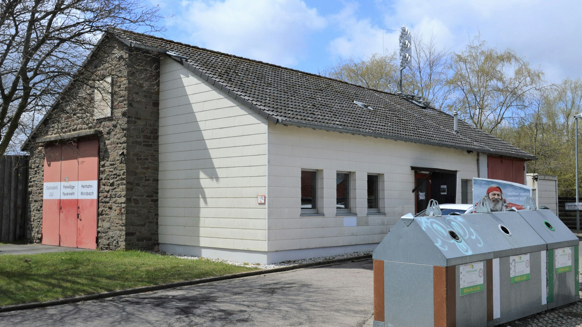 Das Bild zeigt ein altes Gebäude, davor stehen mehrere Flaschencontainer.