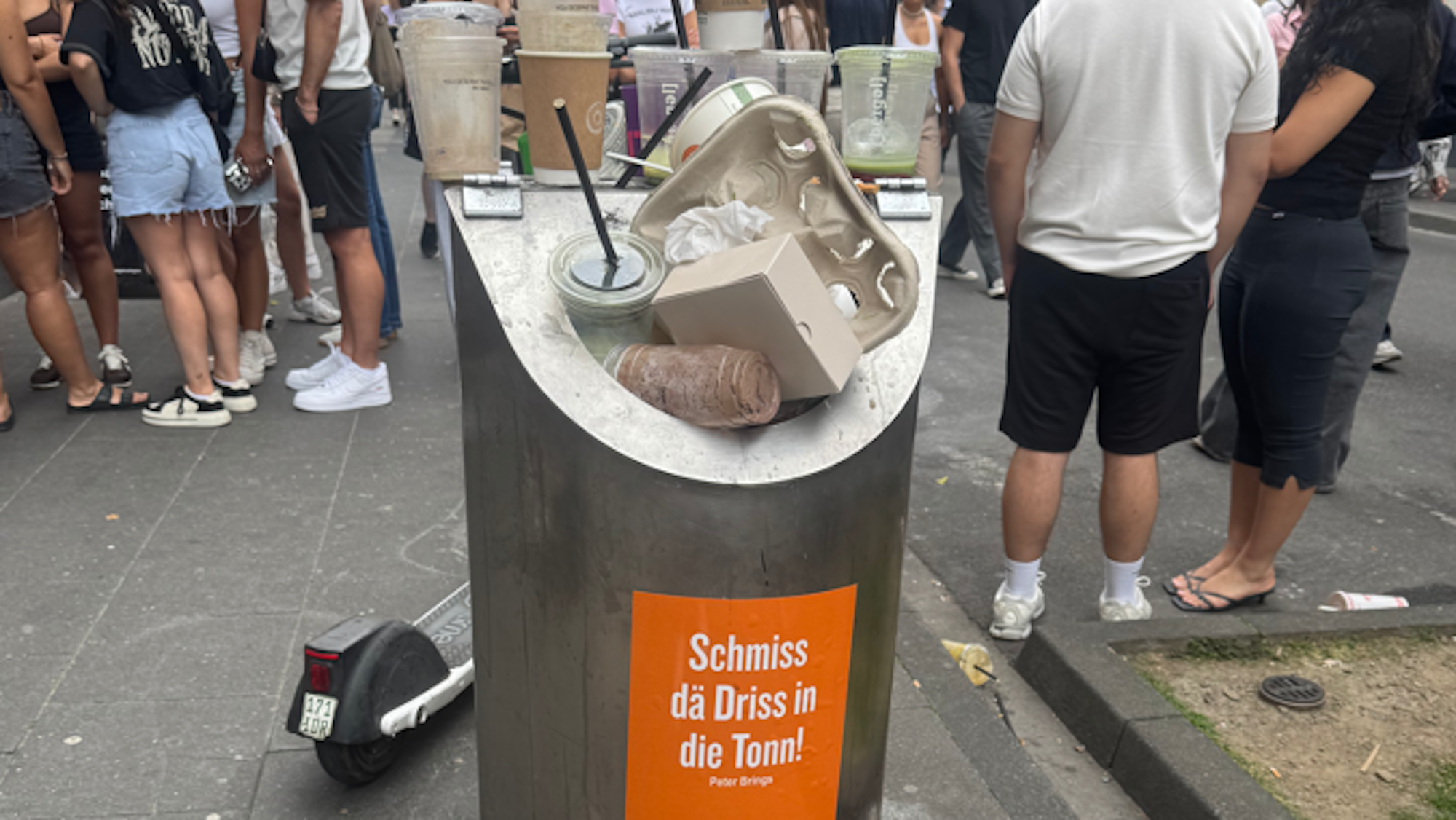 Ein überfüllter öffentlicher Papierkorb auf der Ehrenstraße. Daneben liegen Müllsäcke und Verpackungen auf dem Gehweg.