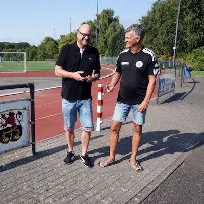 Vorsitzender Andre Vicariesmann und Geschäftsführer Jörg Müller stehen an einem Sportplatz.