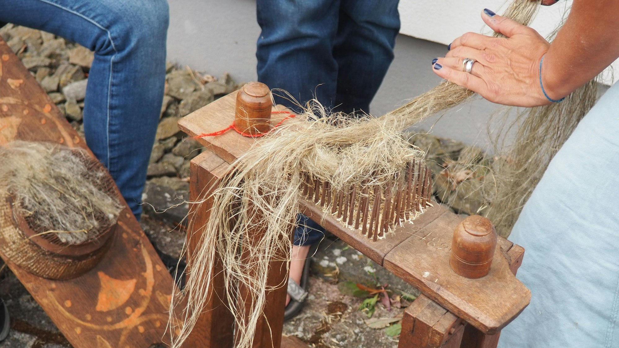 Auf einem hölzernen Gestell sind Spitzen angebracht. Eine Hand zieht die Fasern darüber, um sie von holzigen Teilen zu befreien.