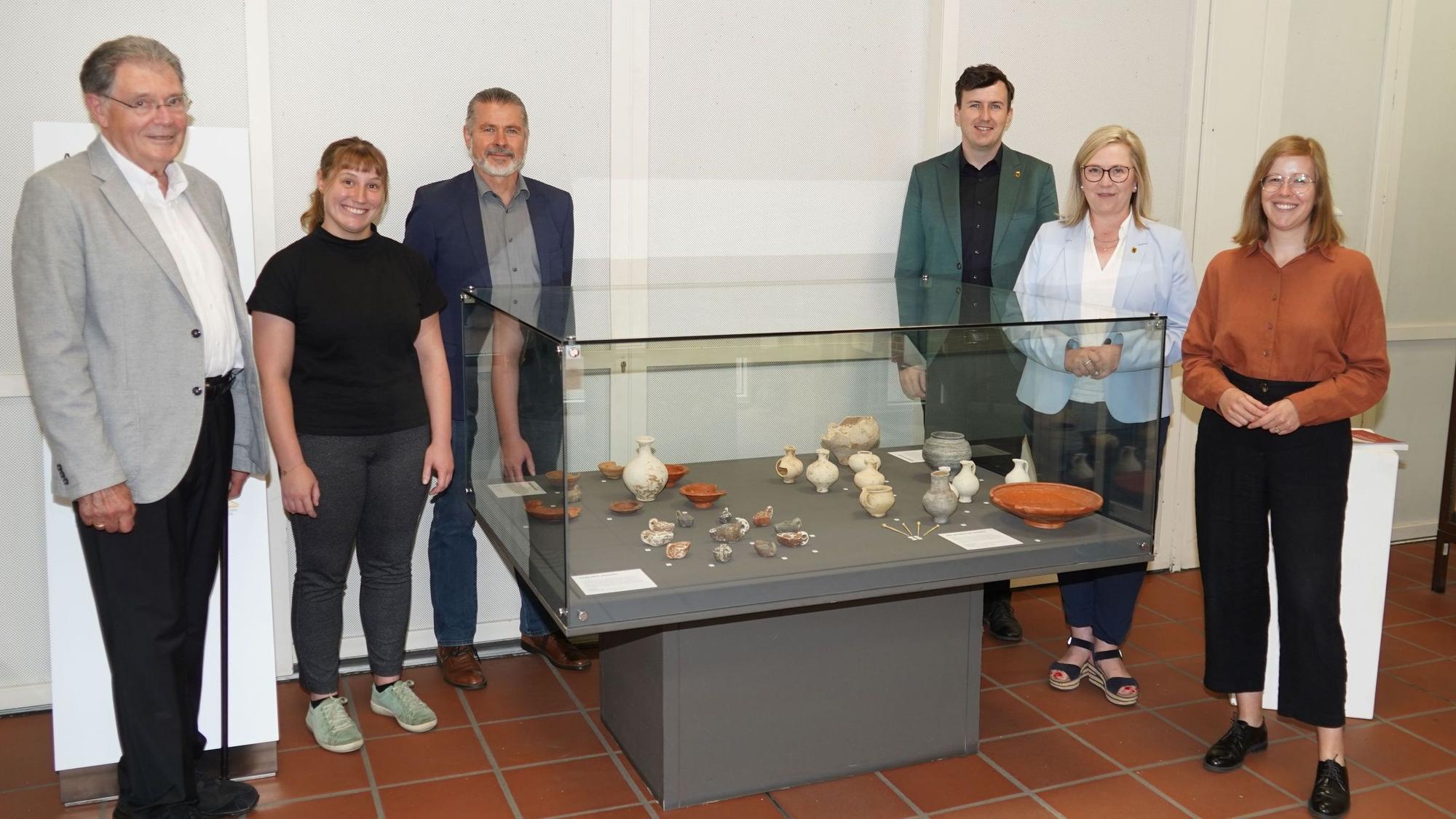 Auf dem Bild ist eine Gruppe von Männern und Frauen neben einer Ausstellungsvitrine zu sehen.