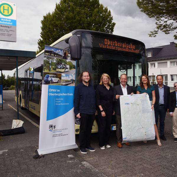 Fünf Menschen stehen am Bahnhof in Waldbröl vor einem Bus und halten ein Plakat hoch.